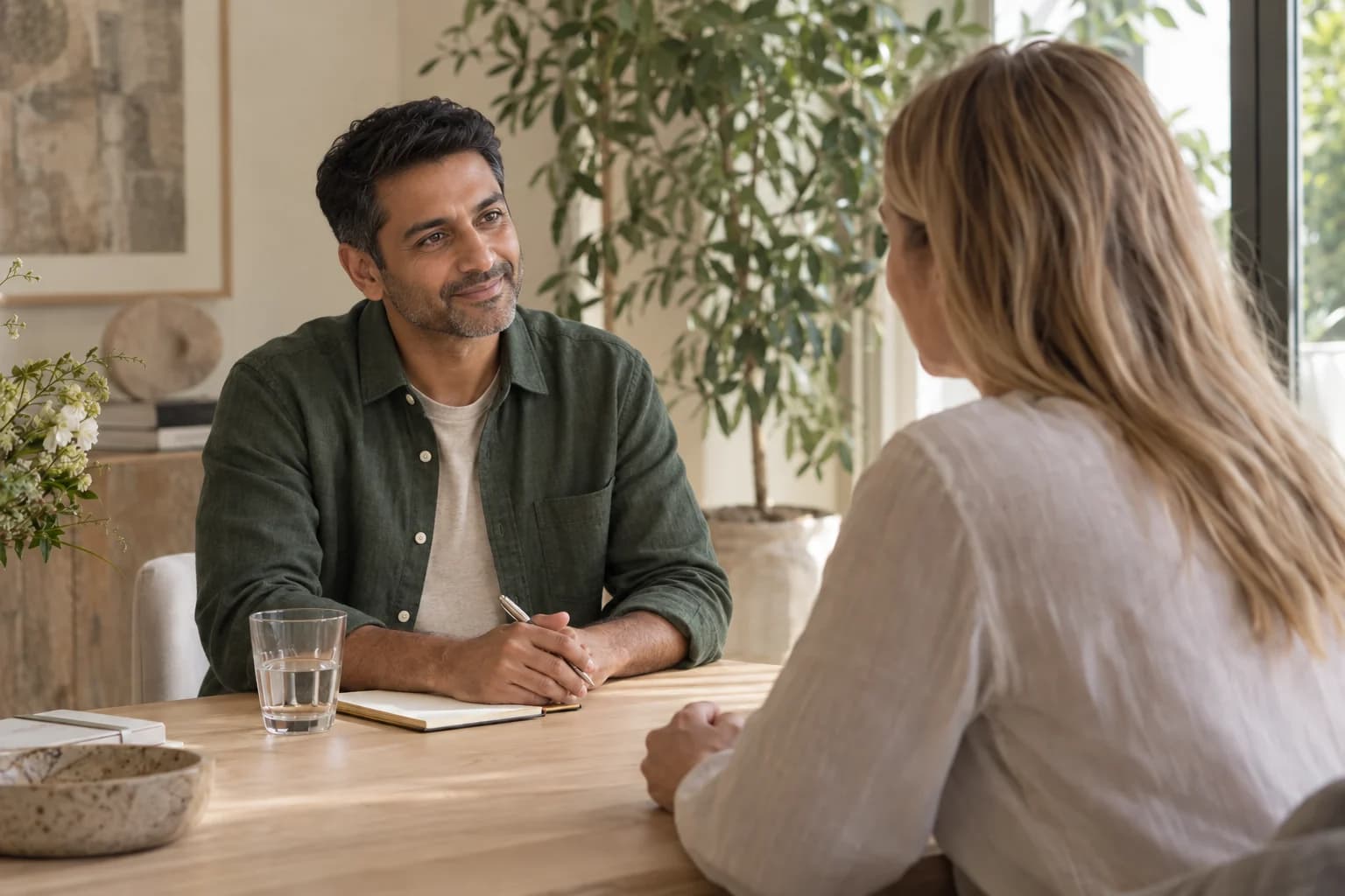 A male practitioner listening to a female client in a warm, light-filled wellbeing space